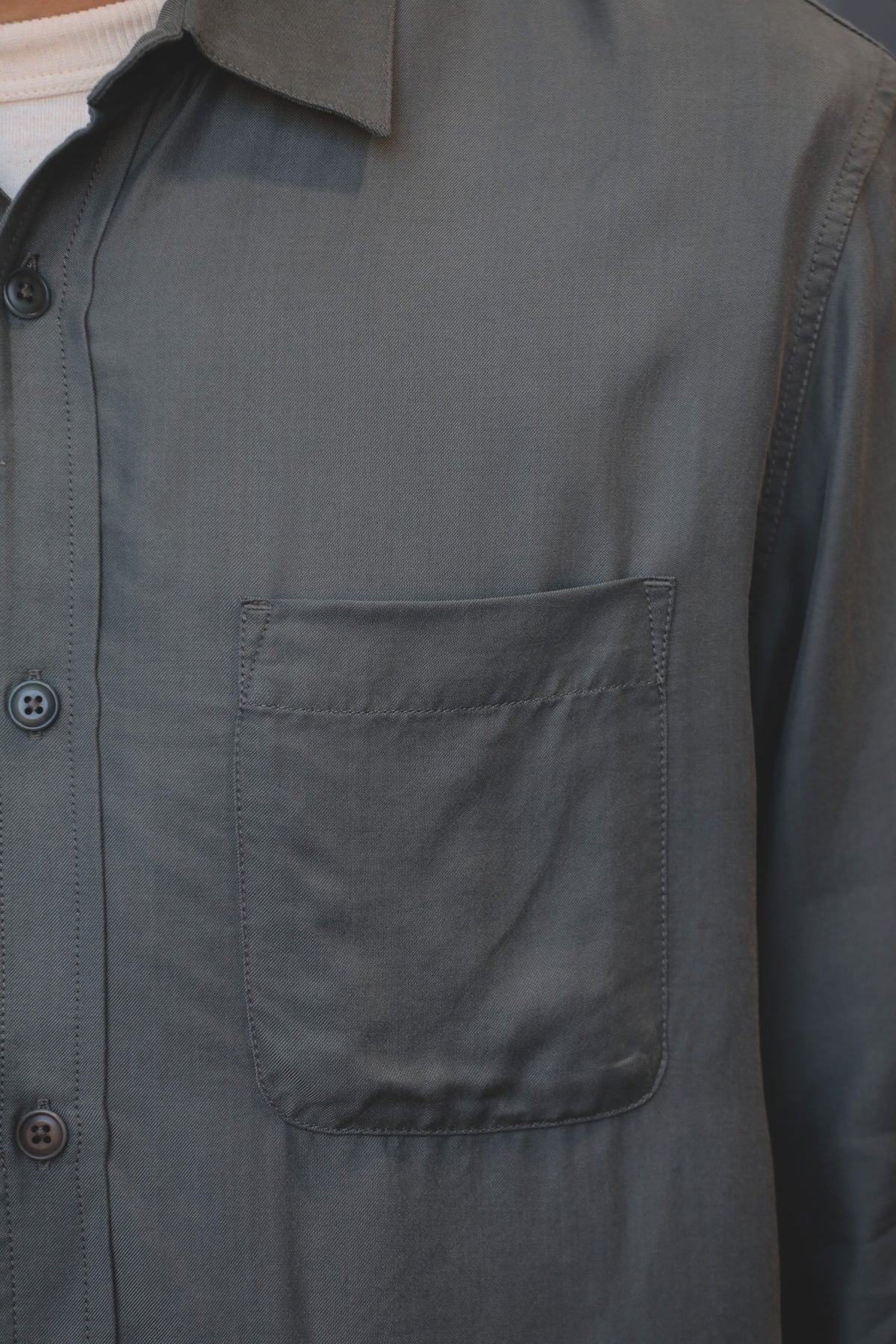 Close-up of a dark gray button-down shirt with a chest pocket, worn over a white undershirt.