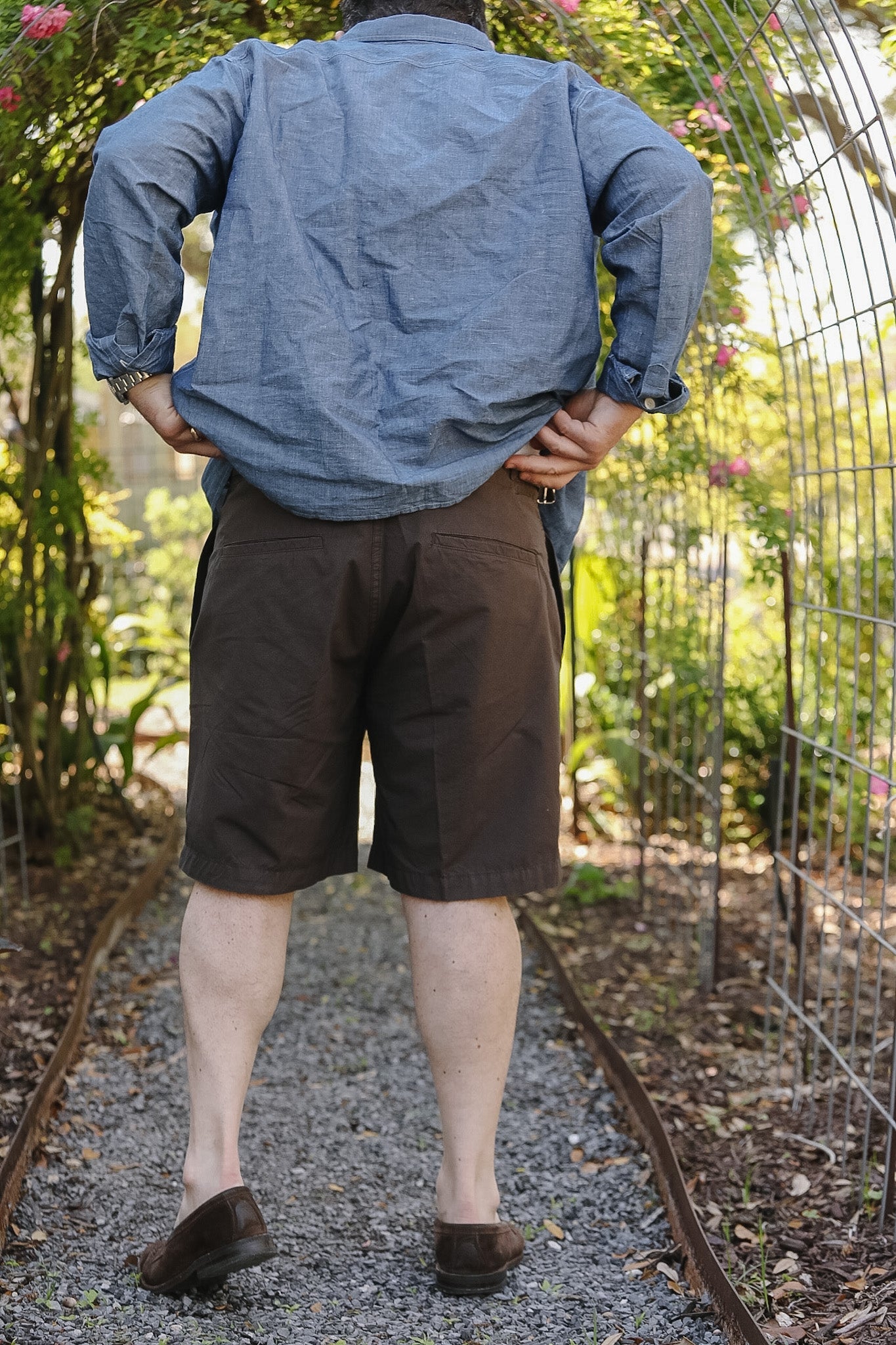 Person wearing a blue shirt and brown shorts standing outdoors with greenery in the background
