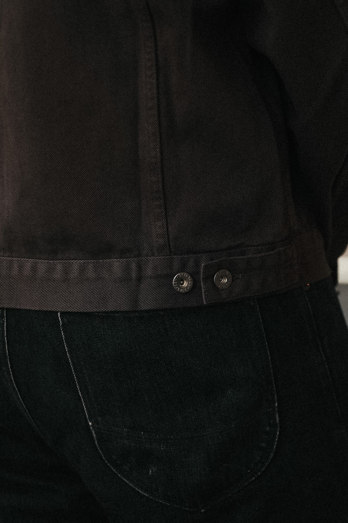 Close-up of a dark brown cropped jacket with a buttoned waistband, worn over black jeans.