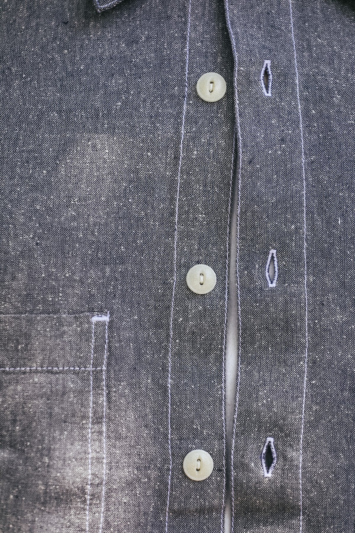 Close-up of a dark gray textured button-up shirt with cream-colored buttons and white contrast stitching.