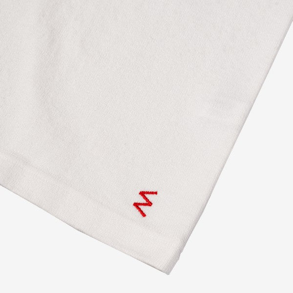 Close-up of white fabric with small red embroidered 'M' detail, minimalist textile design