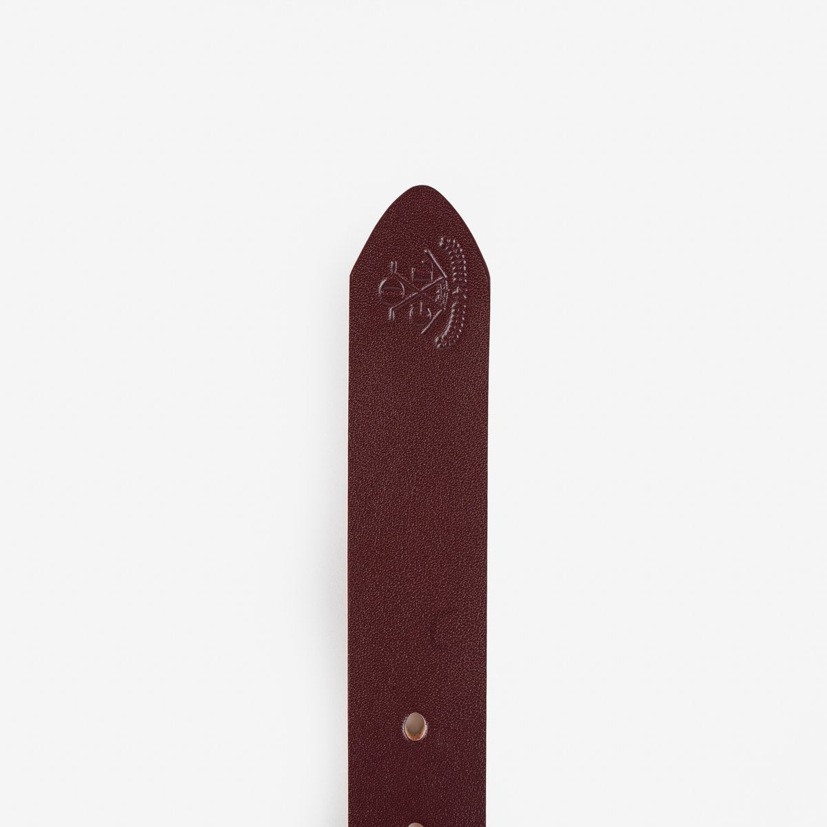 Close-up of burgundy leather belt tip with embossed Iron Shop Provisions logo and punched holes on white background