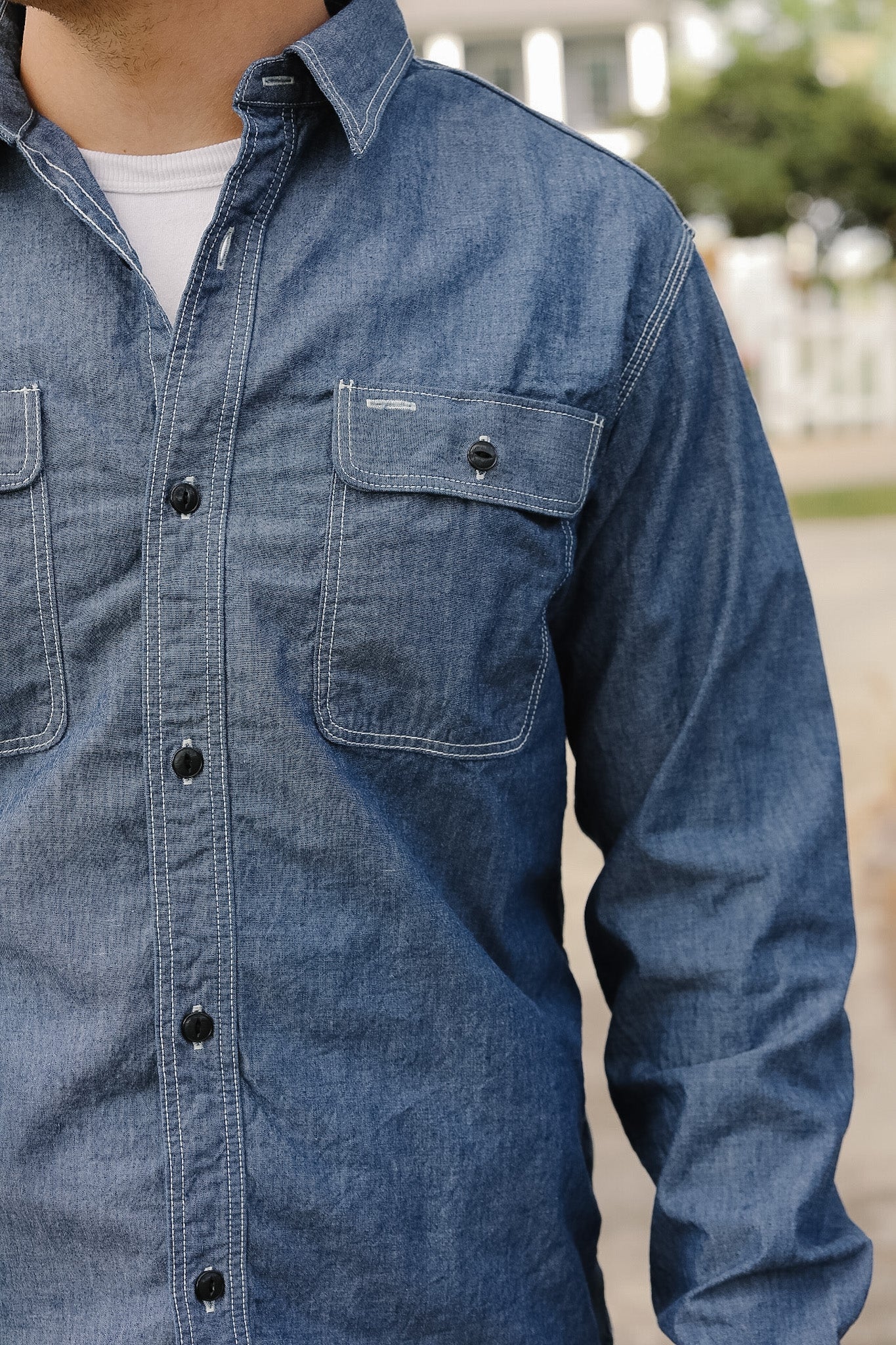 Blue denim shirt worn by a person with a blurred outdoor background