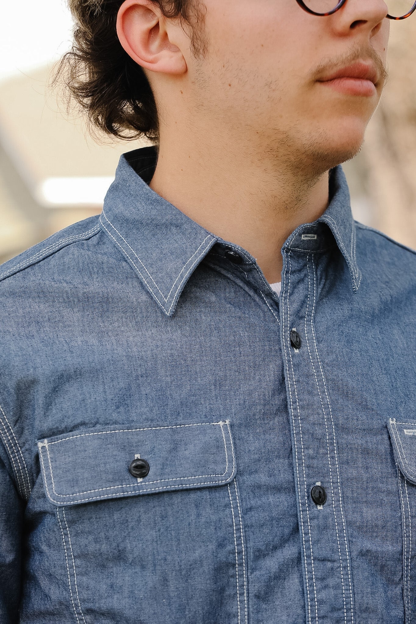 Close-up of a person wearing a blue denim shirt with a blurred background