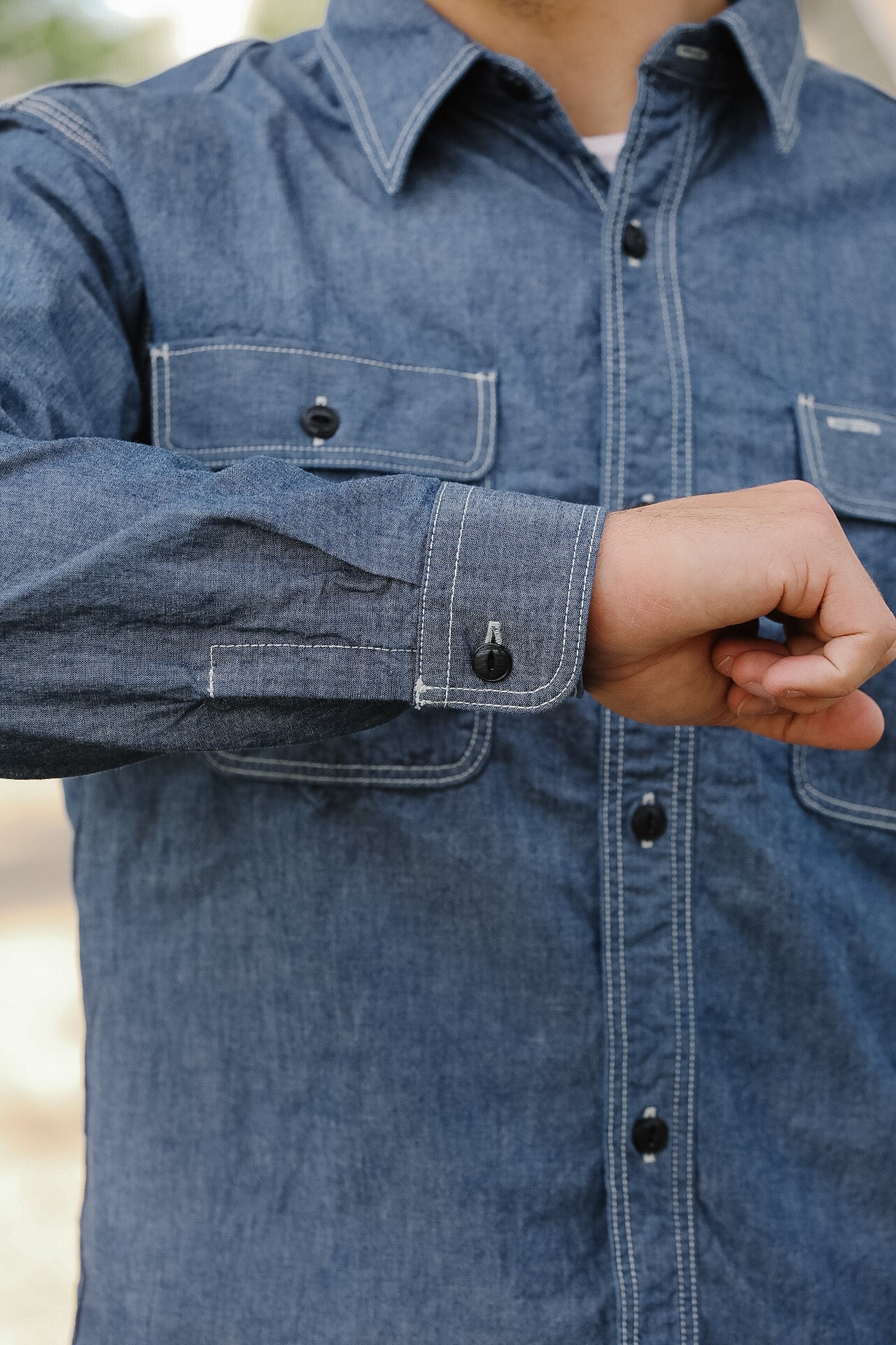 Close-up of a person wearing a blue denim shirt with a blurred background