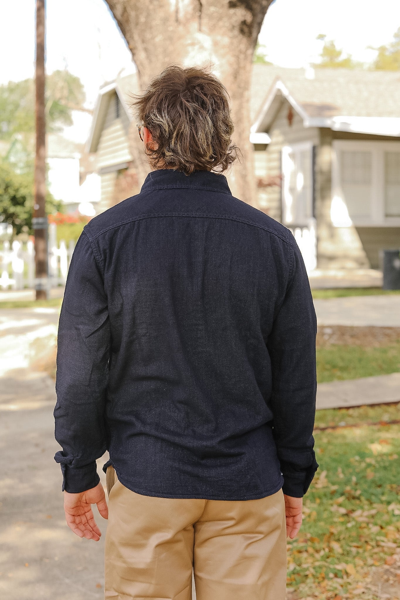 Person wearing a dark blue jacket and beige pants standing outdoors with houses in the background