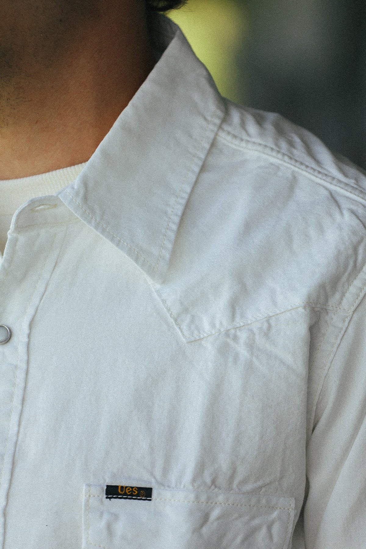 Close-up of a person wearing a white western-style button-up shirt with a pointed collar and a small black U.S.