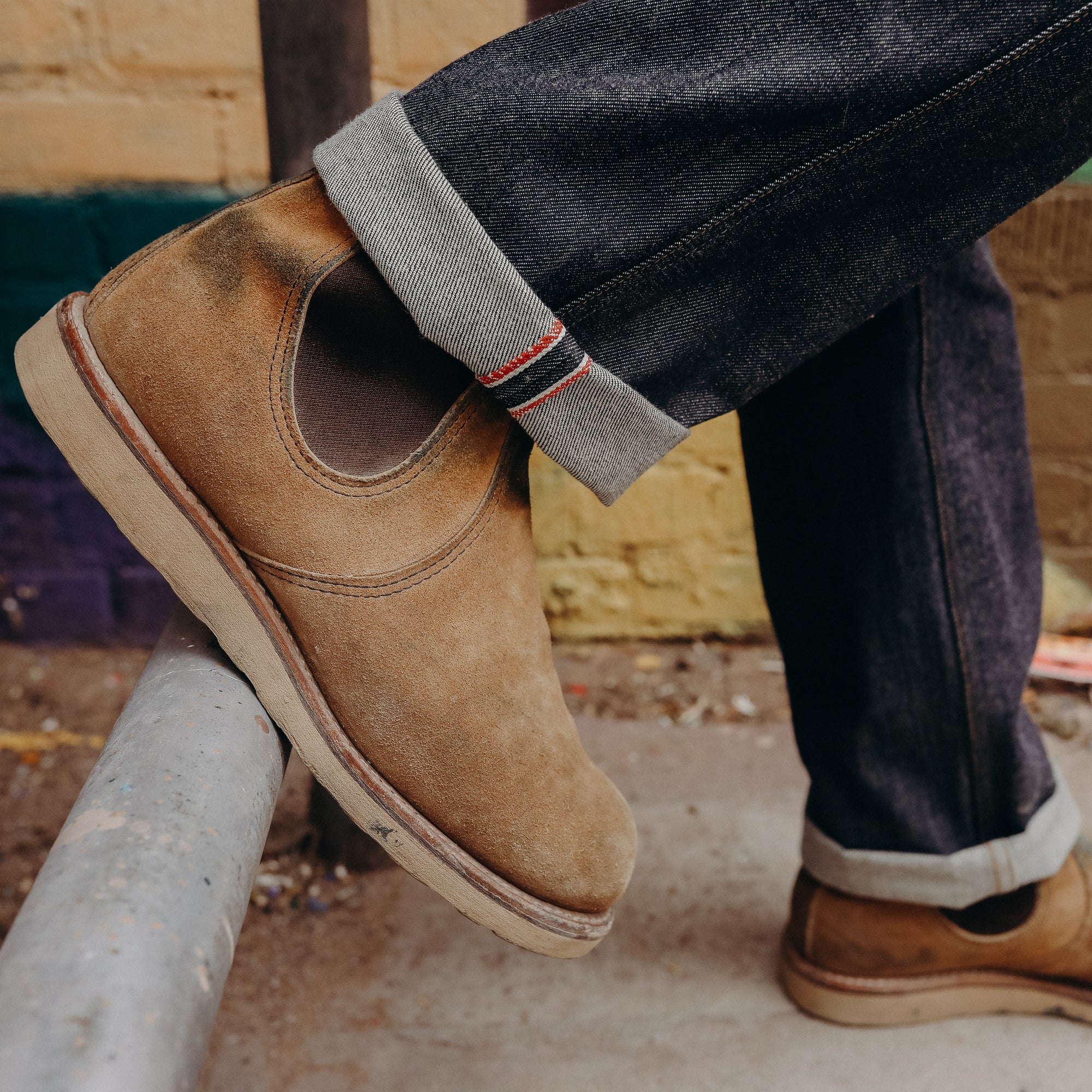 Close-up of tan suede slip-on boots paired with dark rolled-up raw denim jeans outdoors