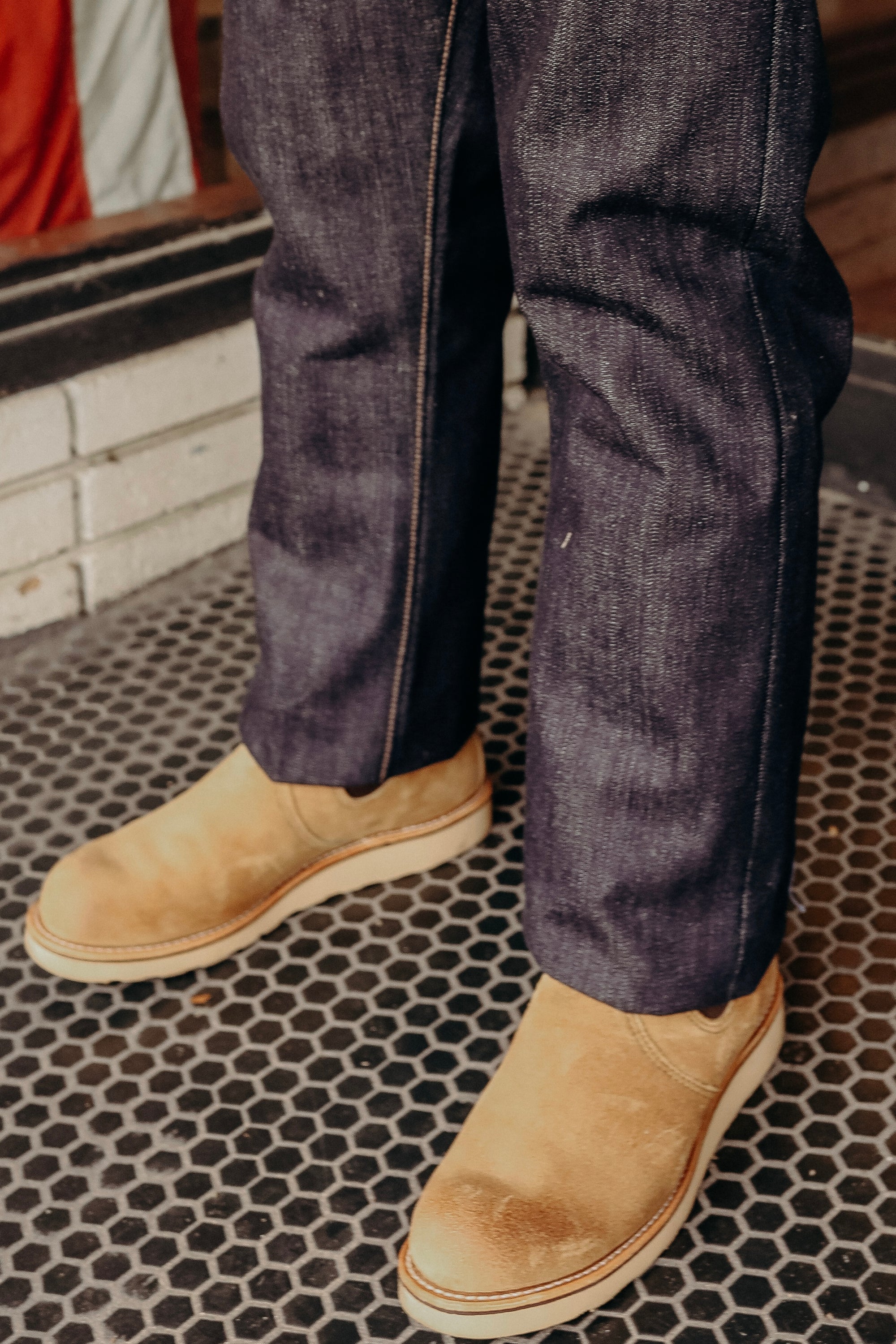 Close-up of tan leather work boots paired with dark blue denim jeans on a hexagonal tile floor