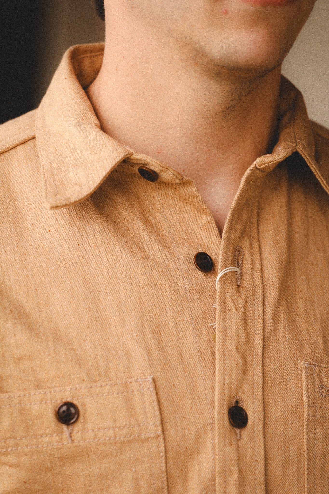 Close-up of a person wearing a beige shirt with black buttons.