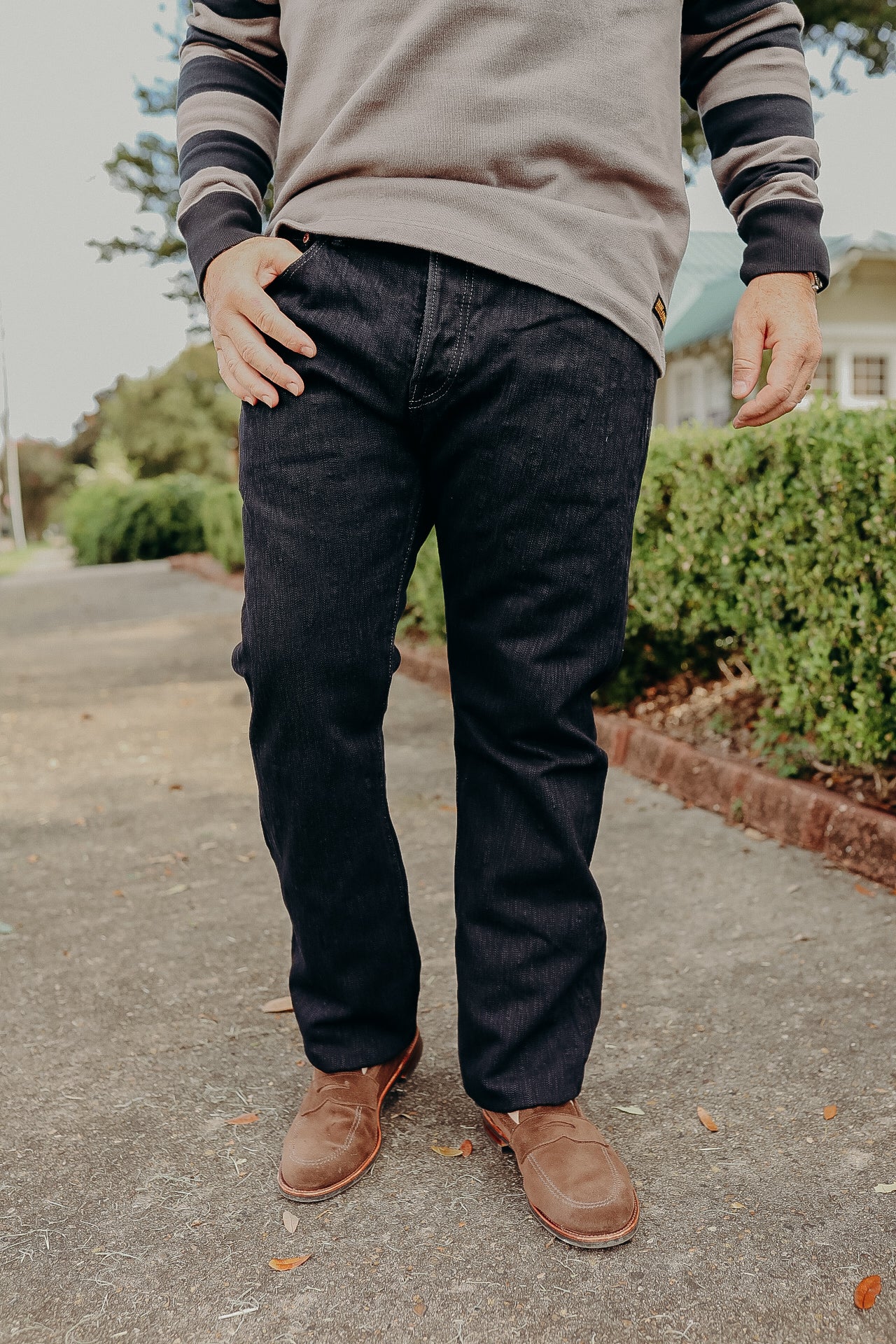 Man wearing dark jeans, brown suede shoes, and a beige and black striped sweater outdoors