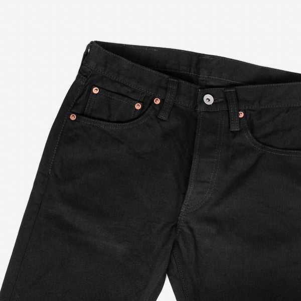 Close-up of black denim jeans with copper rivets and button fly, showcasing front pockets and belt loops