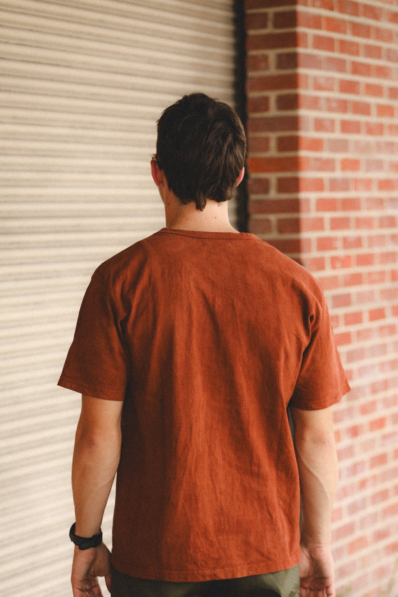Person wearing a brown t-shirt standing in front of a brick wall.