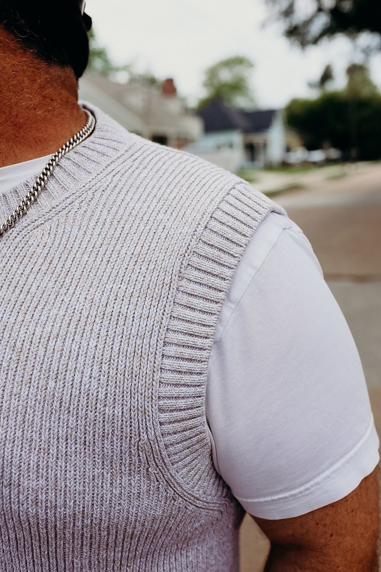 Close-up of a man wearing a silver chain necklace, white T-shirt, and light knit vest outdoors