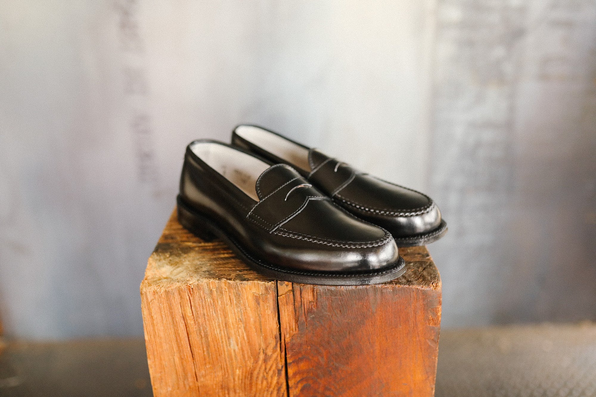 Pair of black loafers on a wooden block with a neutral background