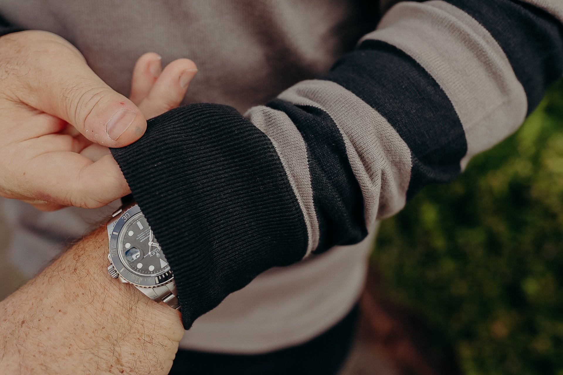 Close-up of a person adjusting a silver luxury wristwatch under a gray and black striped long-sleeve shirt sleeve
