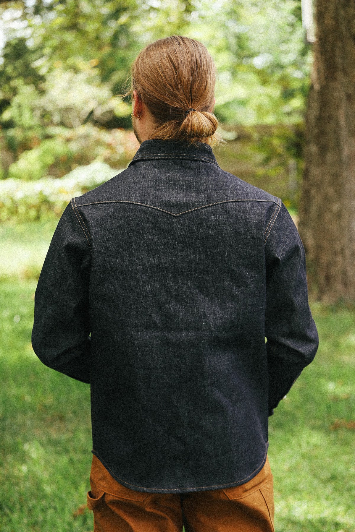 man facing away with denim shirt against a green natural background