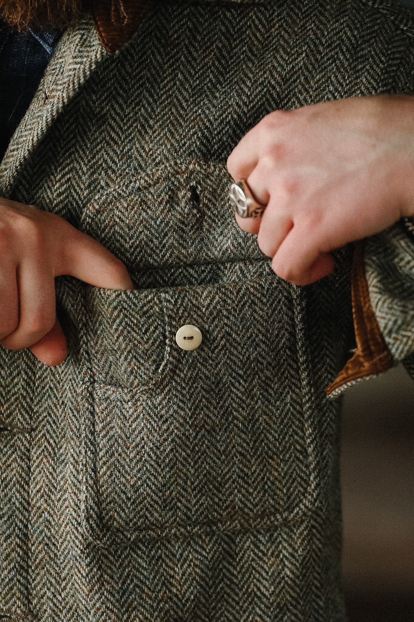 Close-up of a person buttoning a textured coat with a ring on their finger.