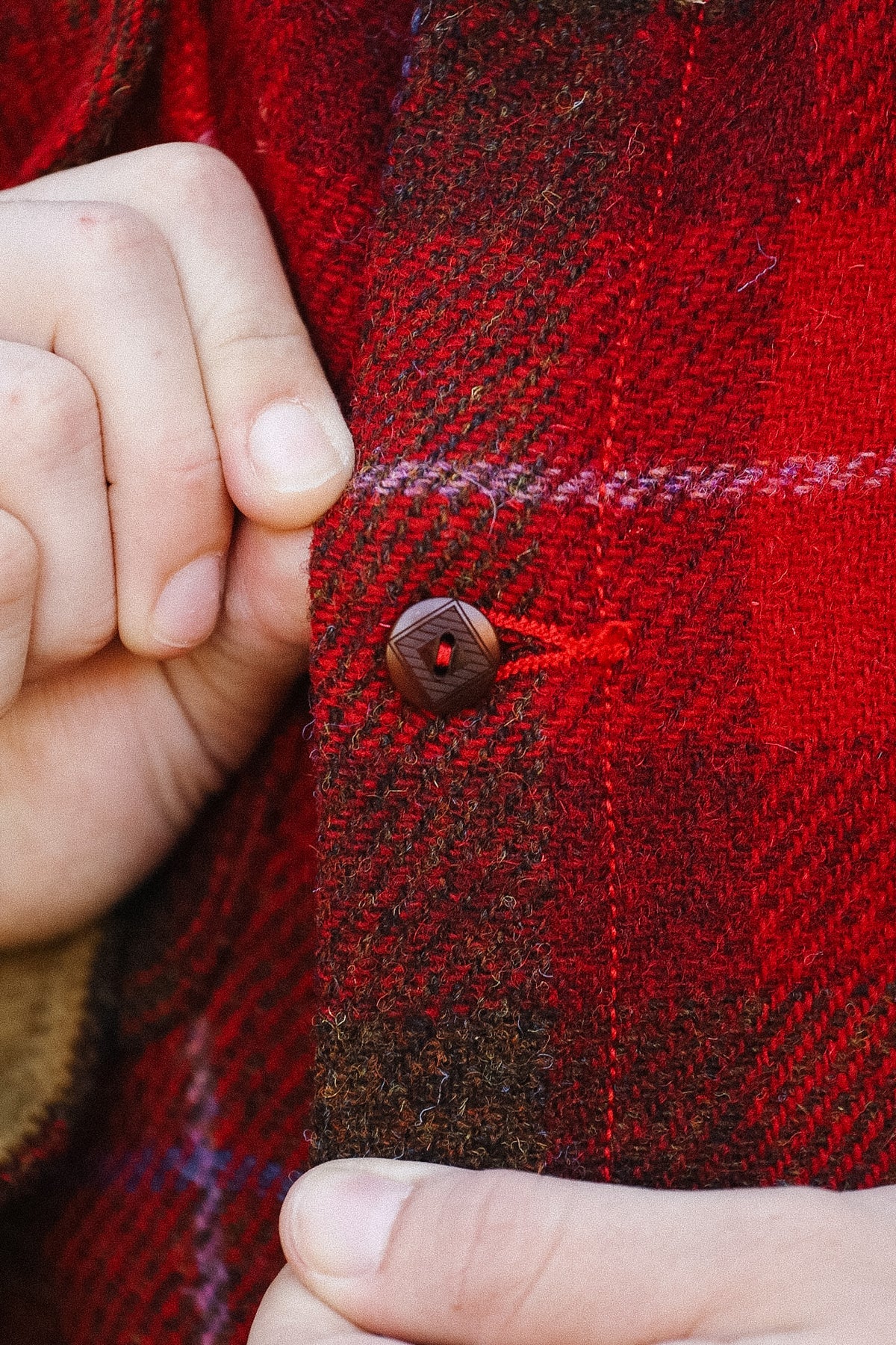 Close-up of a hand buttoning a red plaid jacket
