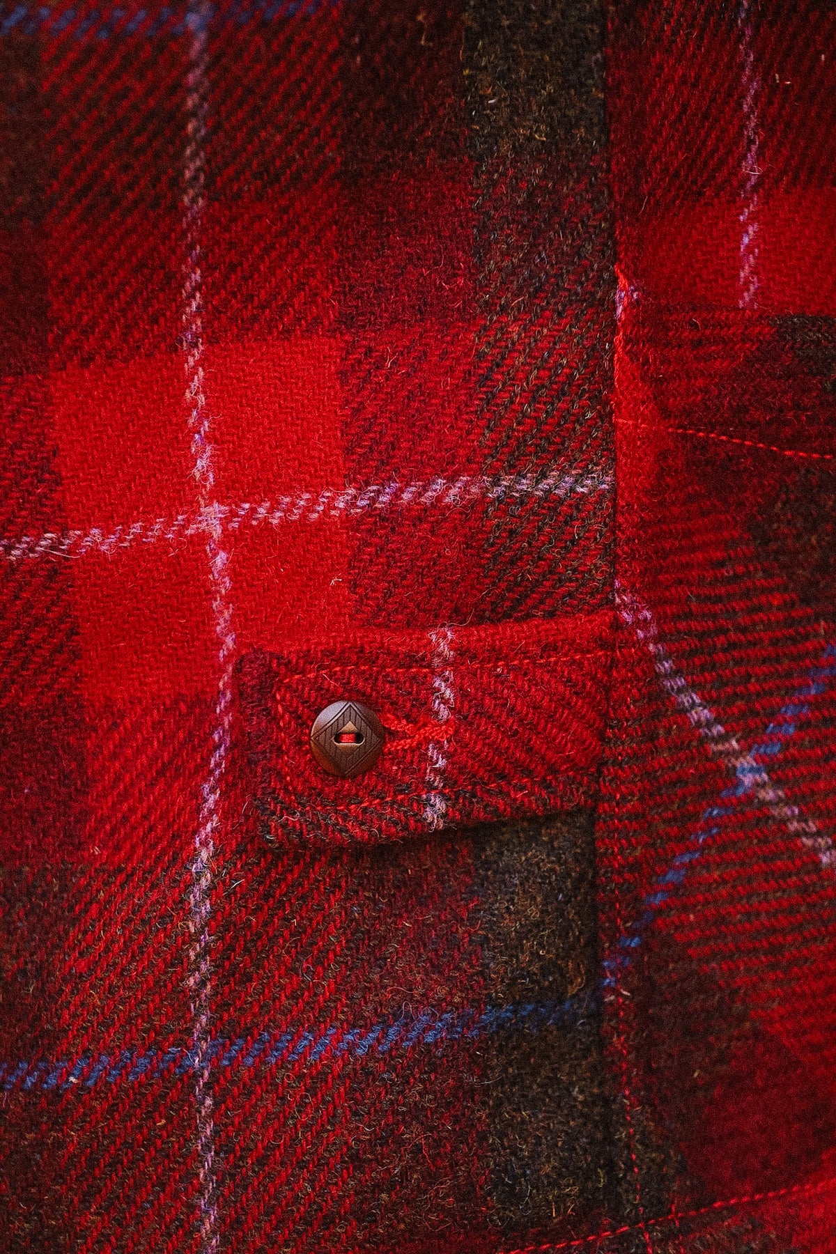 Close-up of a red plaid fabric with a button, showing texture and pattern details.