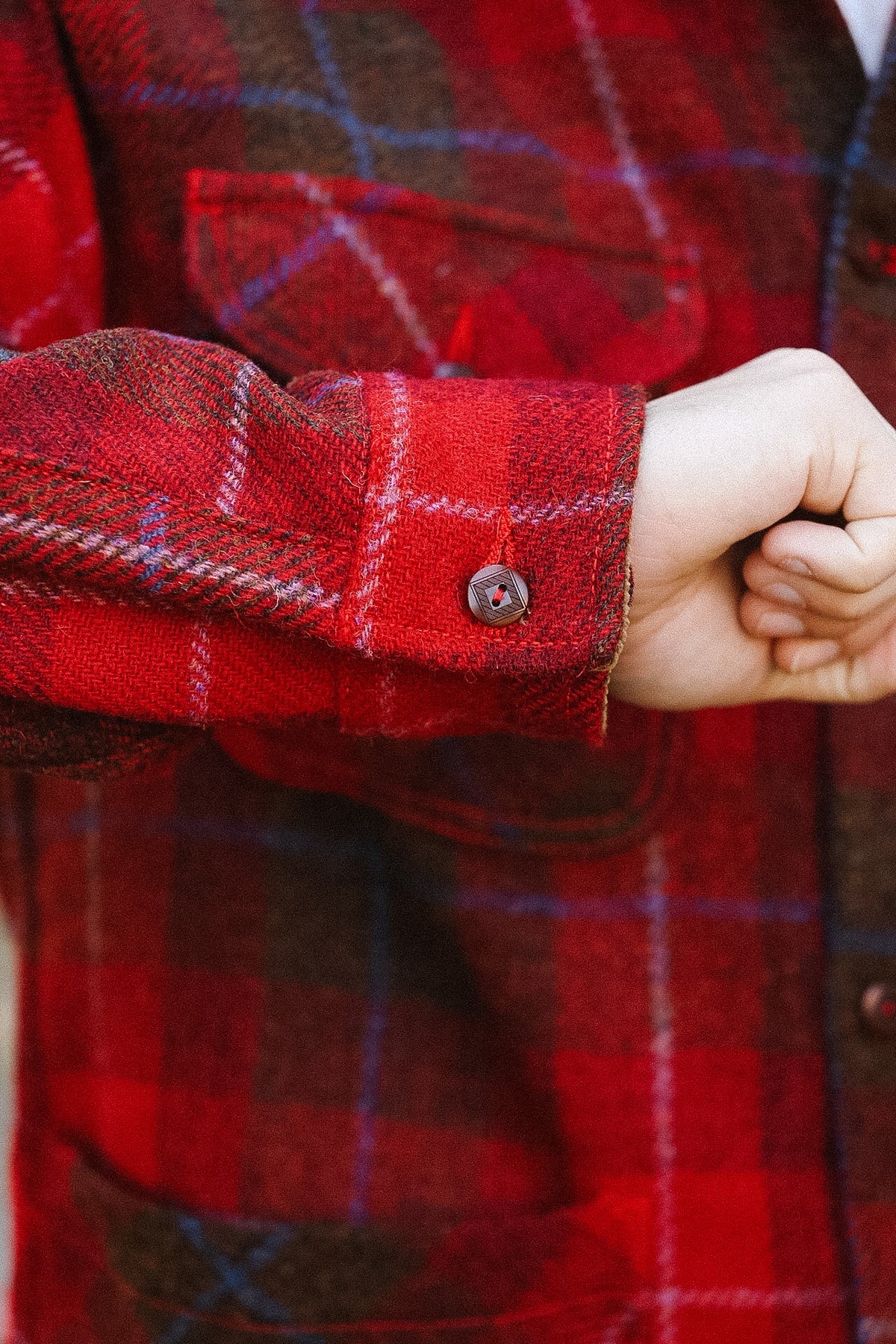 Close-up of a red plaid shirt with a hand adjusting the sleeve.