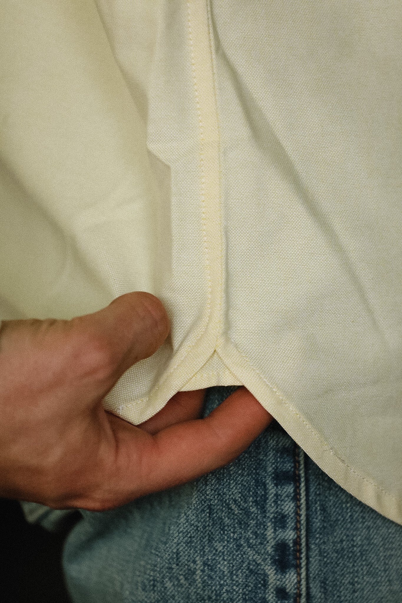 Close-up of a beige fabric with a hand holding it, wearing blue jeans.