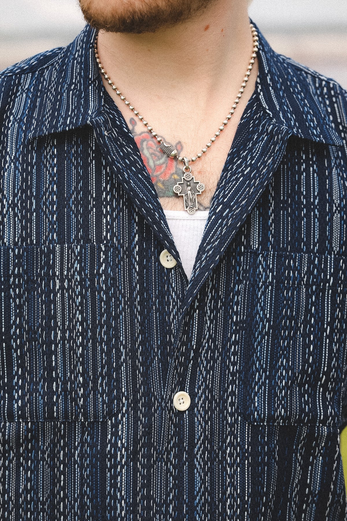 Close-up of a person wearing a dark blue patterned shirt with visible tattoos and jewelry.