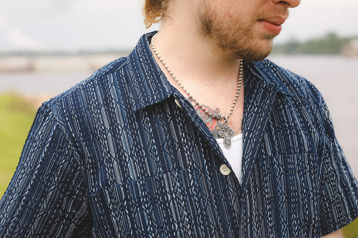 Man wearing a blue patterned shirt with a blurred natural background