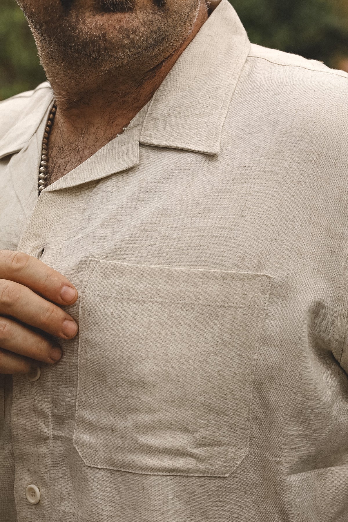 Close-up of a man wearing a light beige linen short-sleeve button-up shirt with a chest pocket, showing the fabric texture and collar.