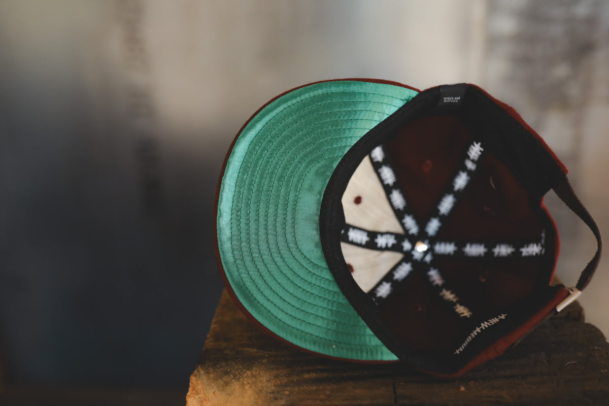 Dark maroon baseball cap on a wood block  with interior branding 
