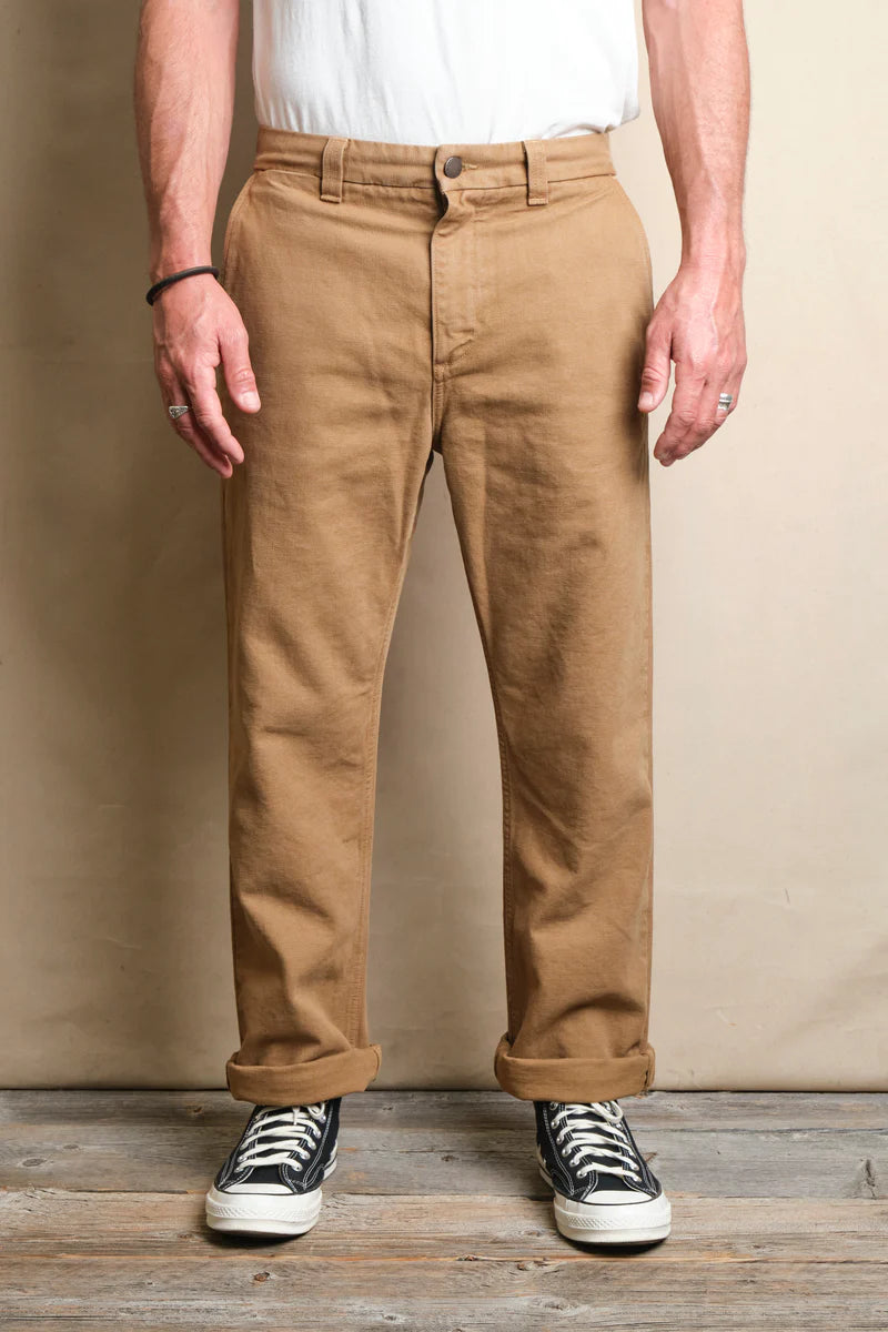 Front view of a man wearing rolled up brown casual pants with black and white sneakers on wooden floor at Iron Shop Provisions