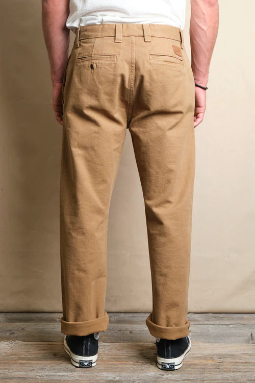 Back view of man wearing beige casual chinos rolled at the ankles with black sneakers on wooden floor