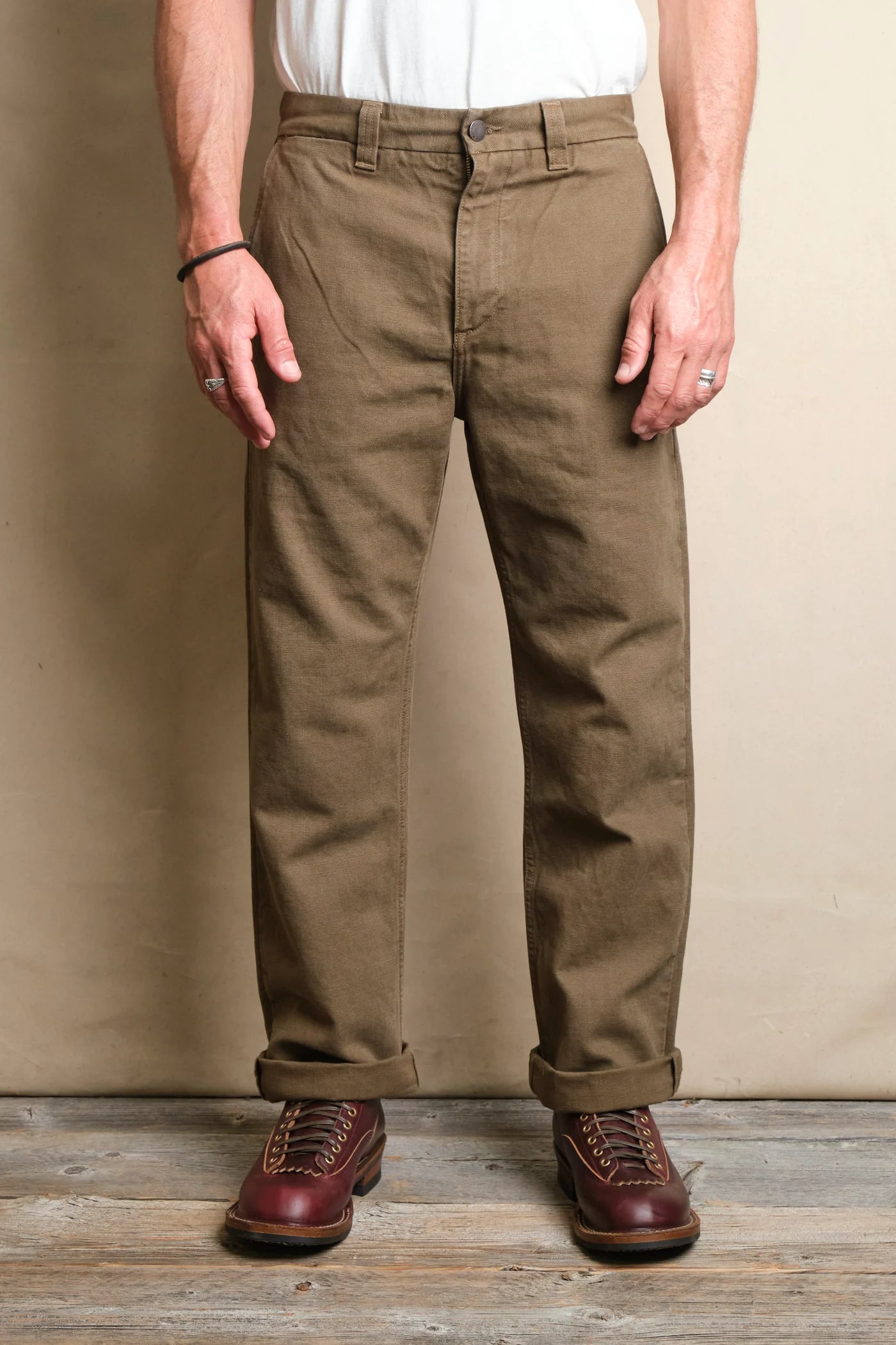 Men's brown work pants paired with rolled cuffs and burgundy leather boots on wooden floor