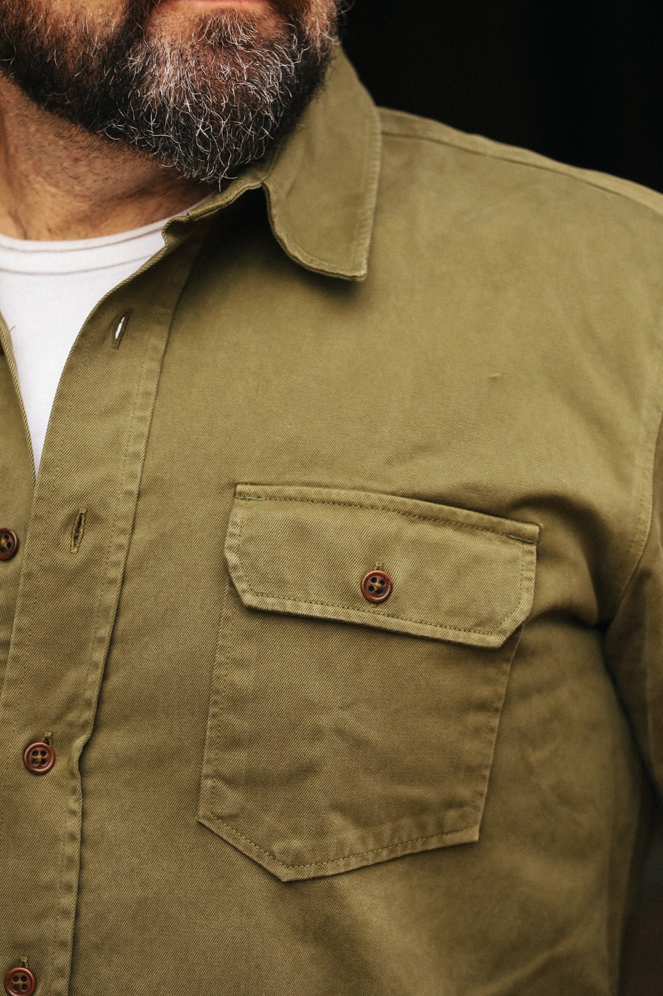 Close-up of a person wearing a green shirt with a pocket and buttons.