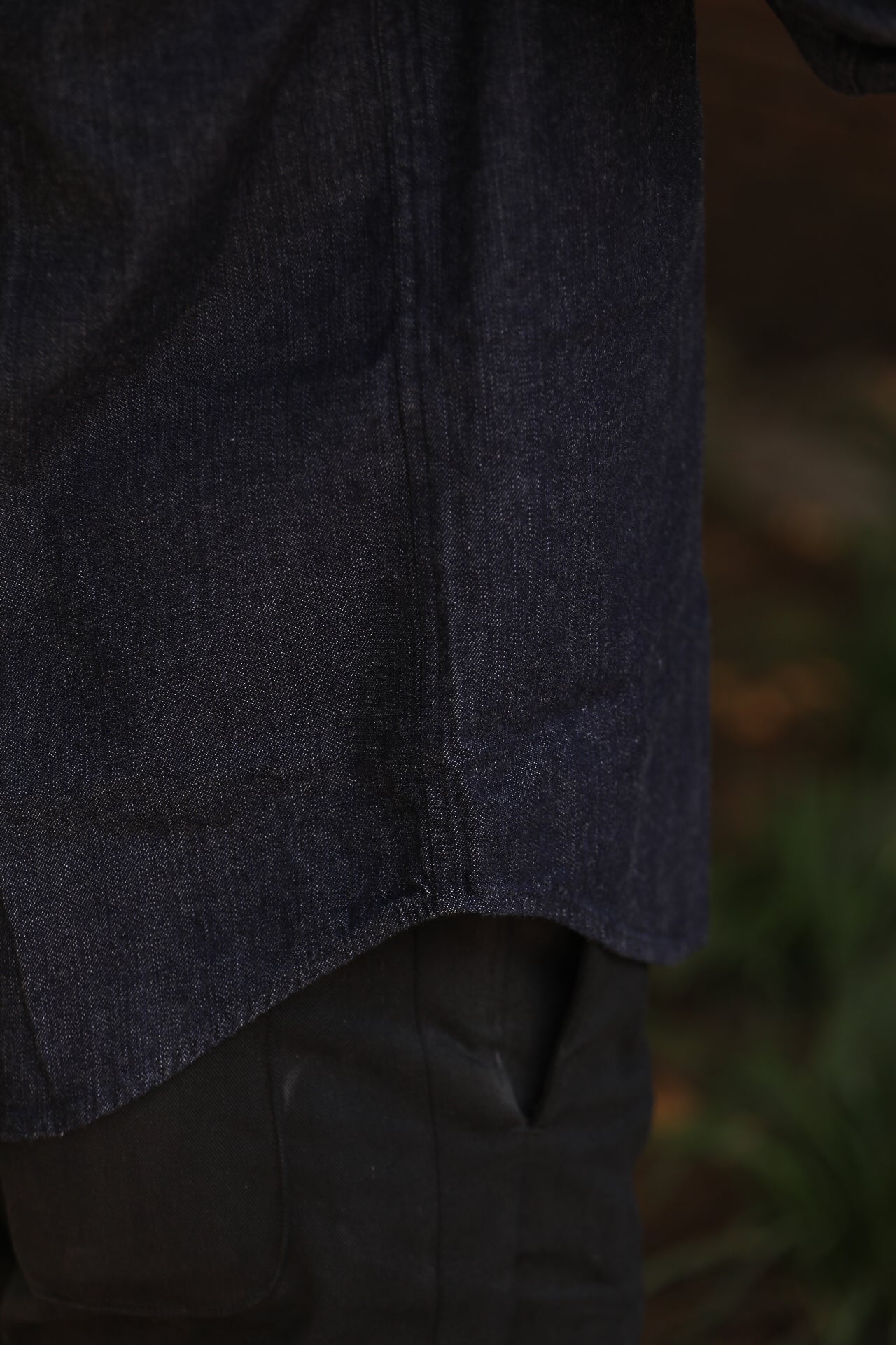 Close-up of dark blue denim shirt hem over black pants in natural outdoor setting