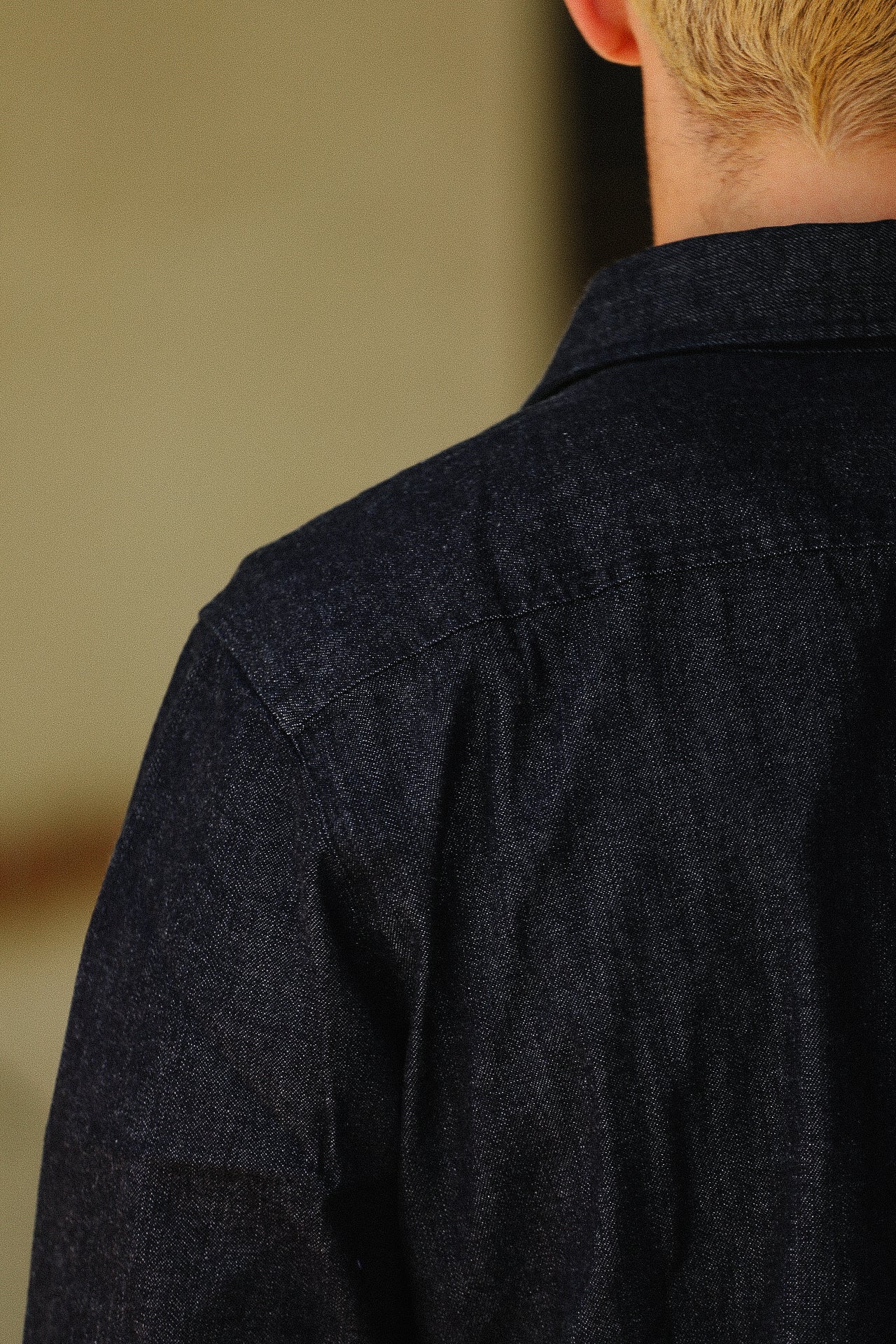 Close-up of a person's back wearing a dark denim jacket with visible stitching