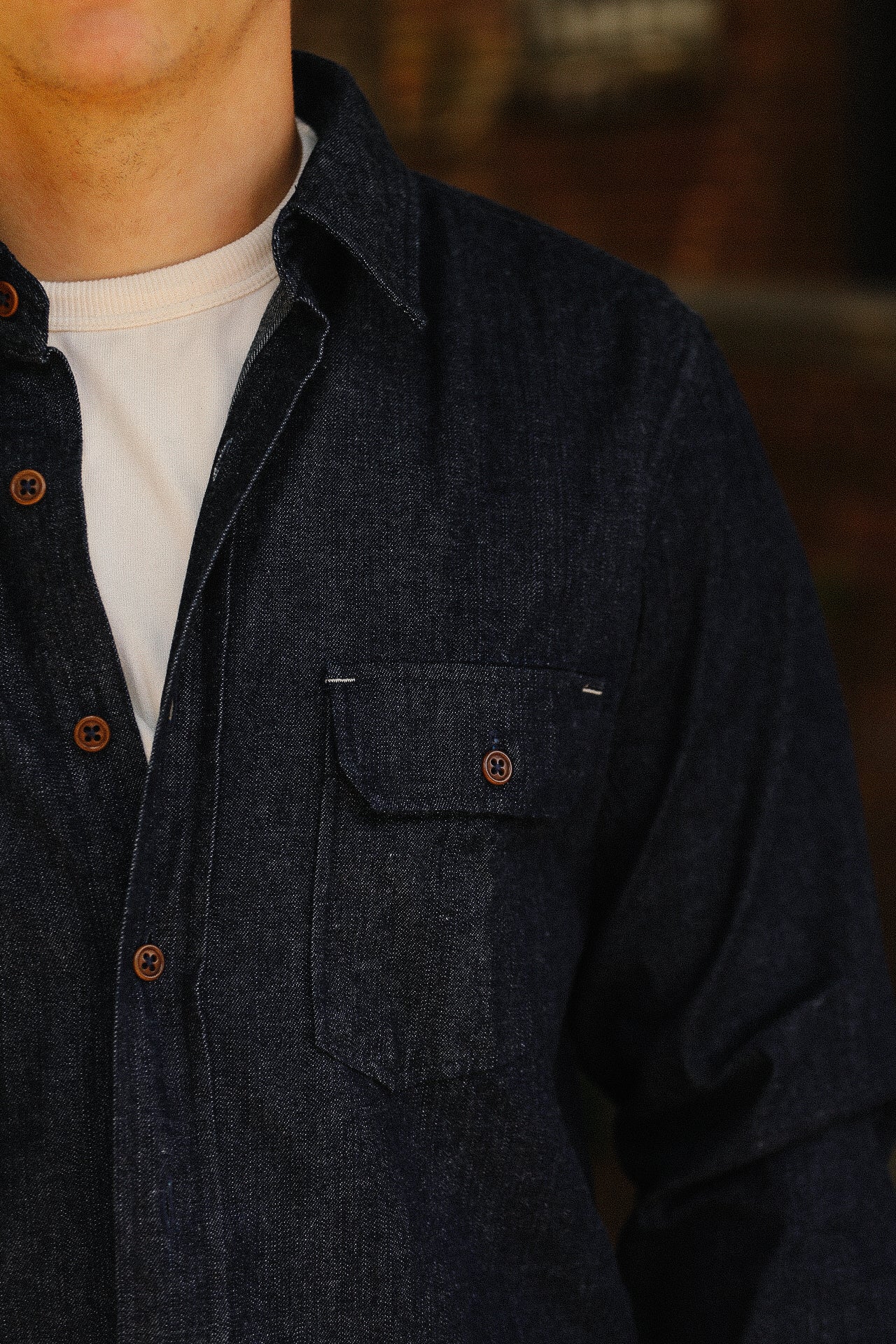 Close-up of man wearing dark denim shirt with brown buttons over white crew neck t-shirt