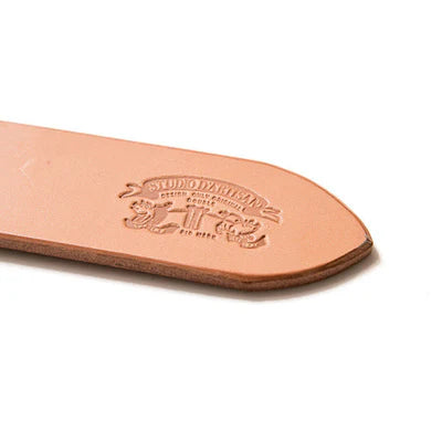 Close-up of natural leather belt tip embossed with Studio D'Artisan logo on white background