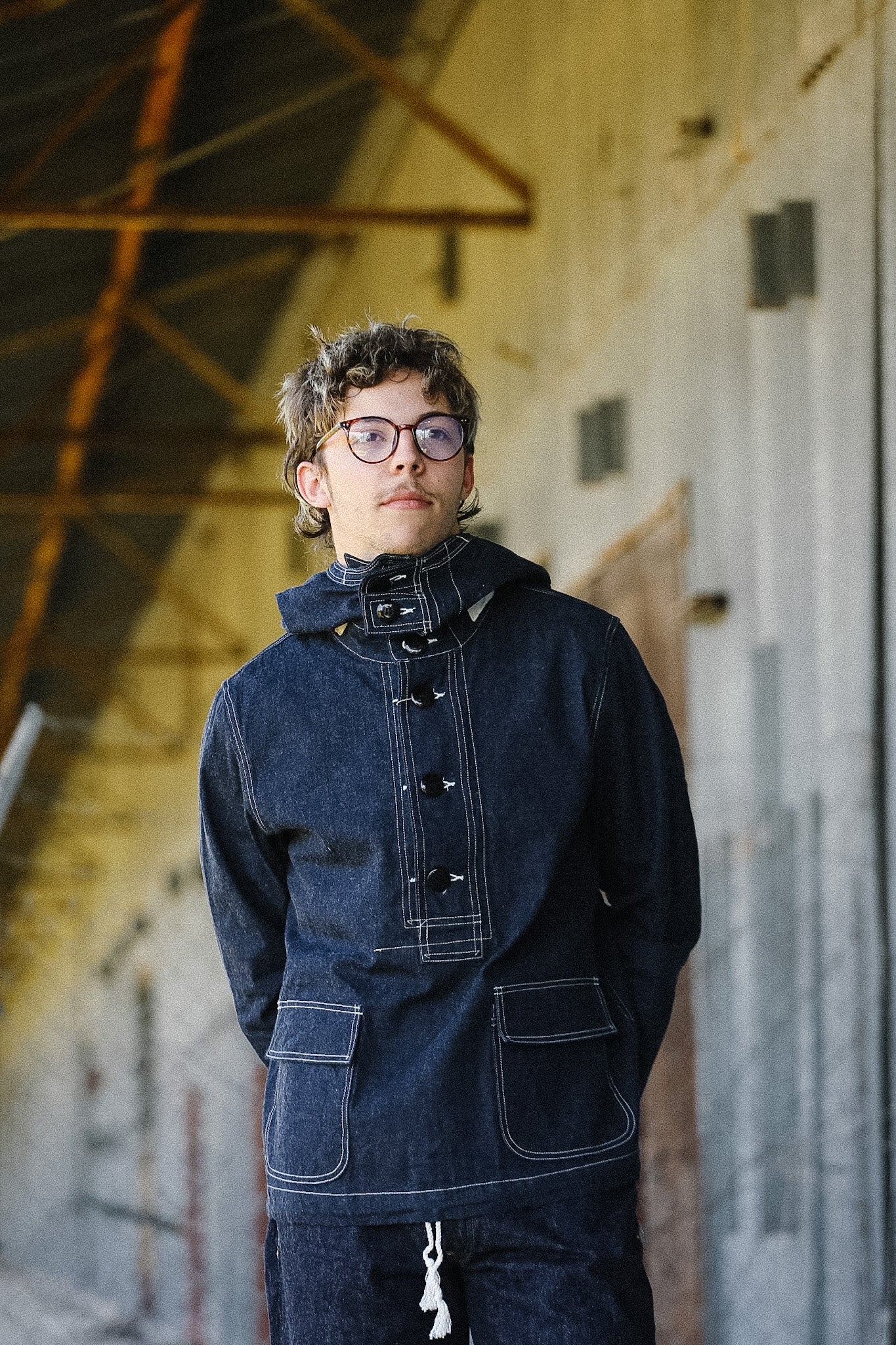 Person wearing a dark denim jacket and pants in an industrial setting