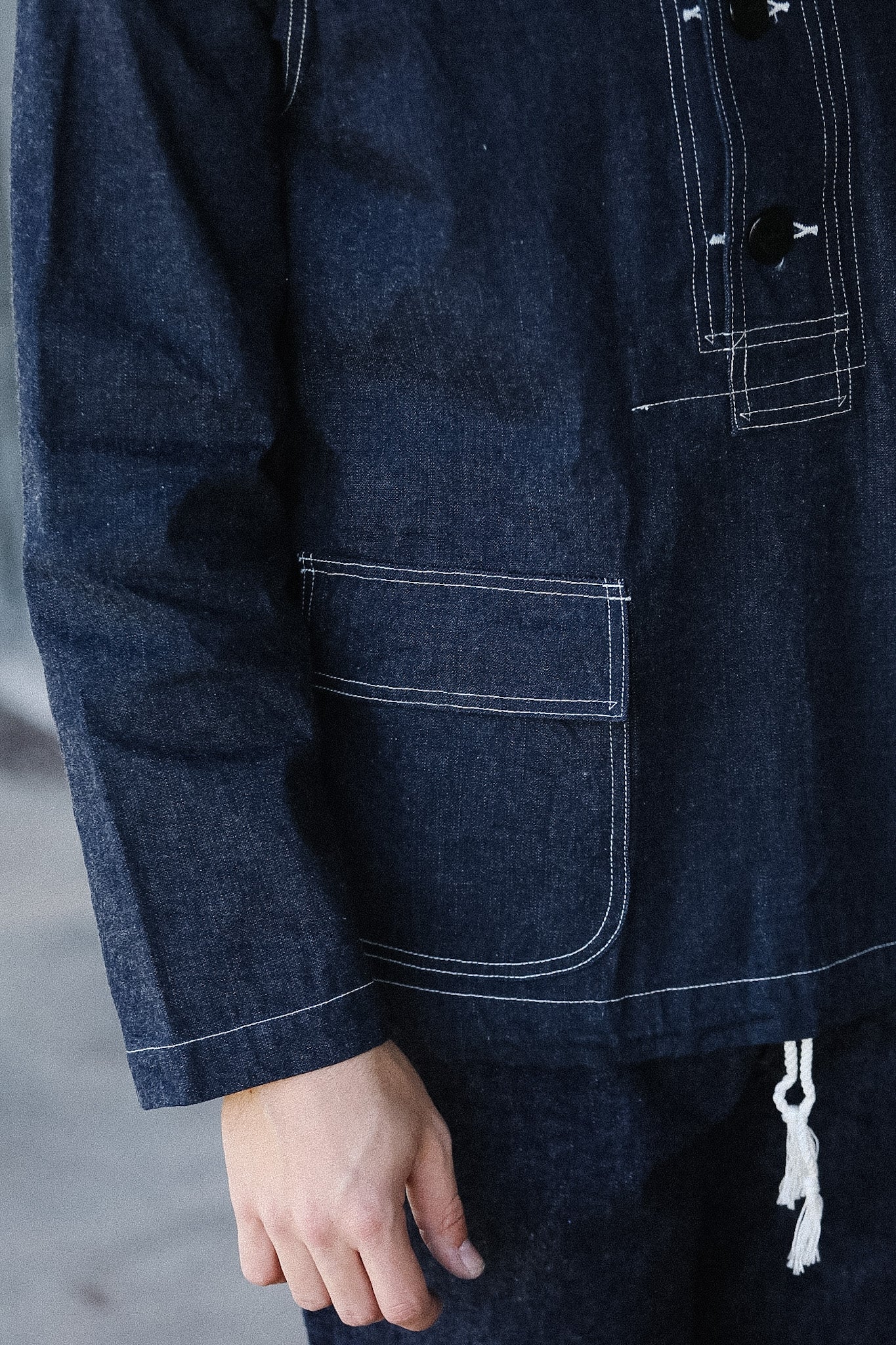 Close-up of a dark blue denim jacket with a pocket and button details.