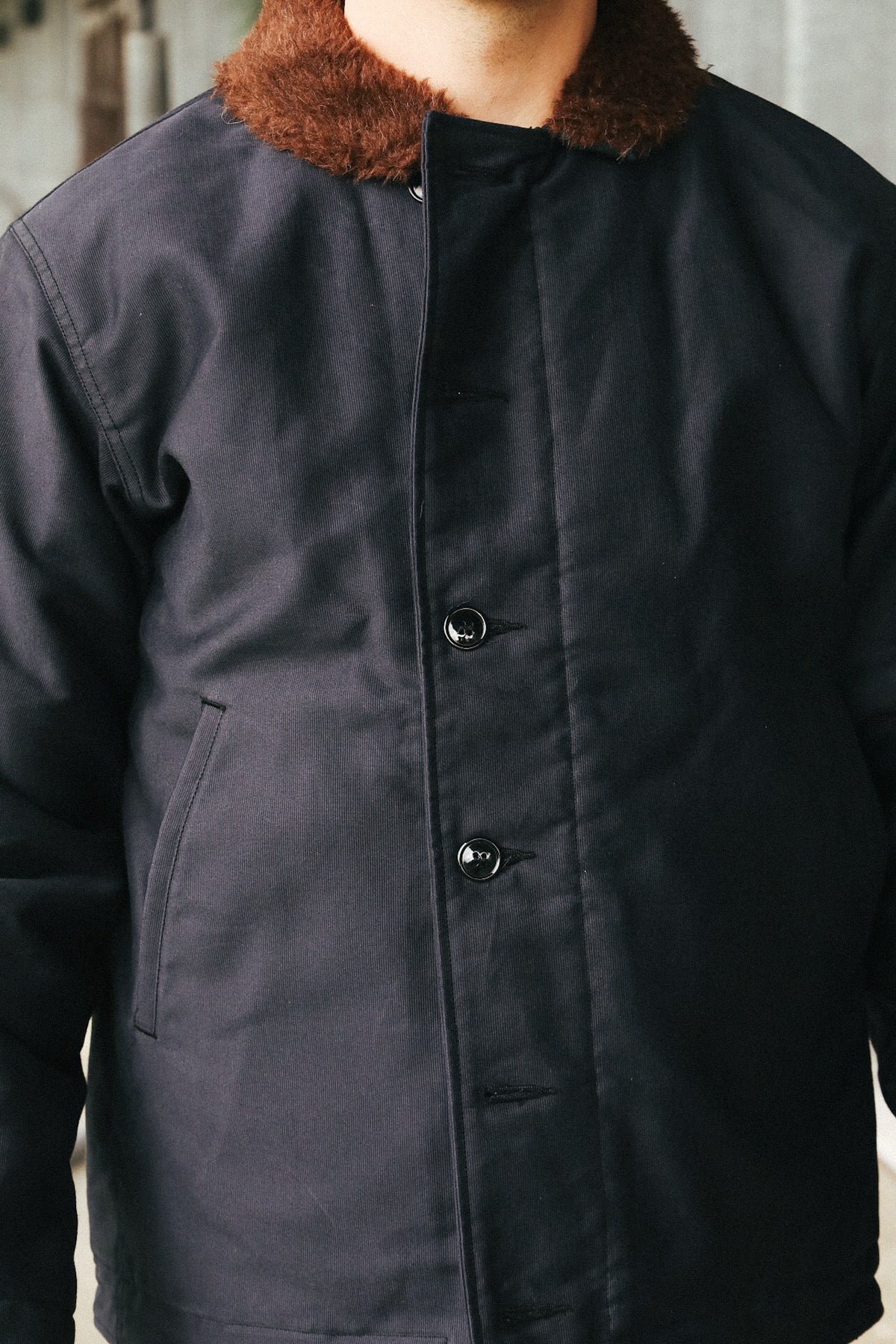 A close-up of a person wearing a dark navy quilted jacket with a brown faux-fur collar and black snap buttons.
