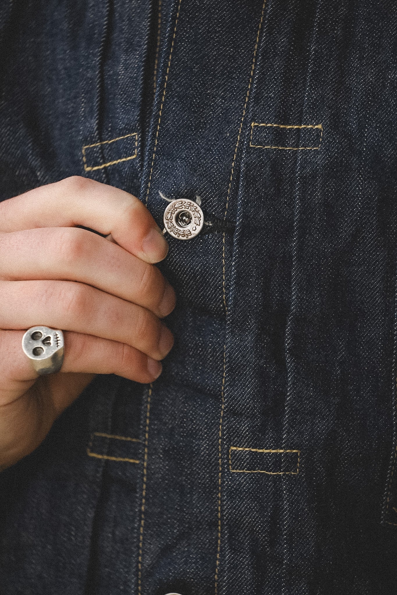 Hand adjusting a button on a dark denim jacket