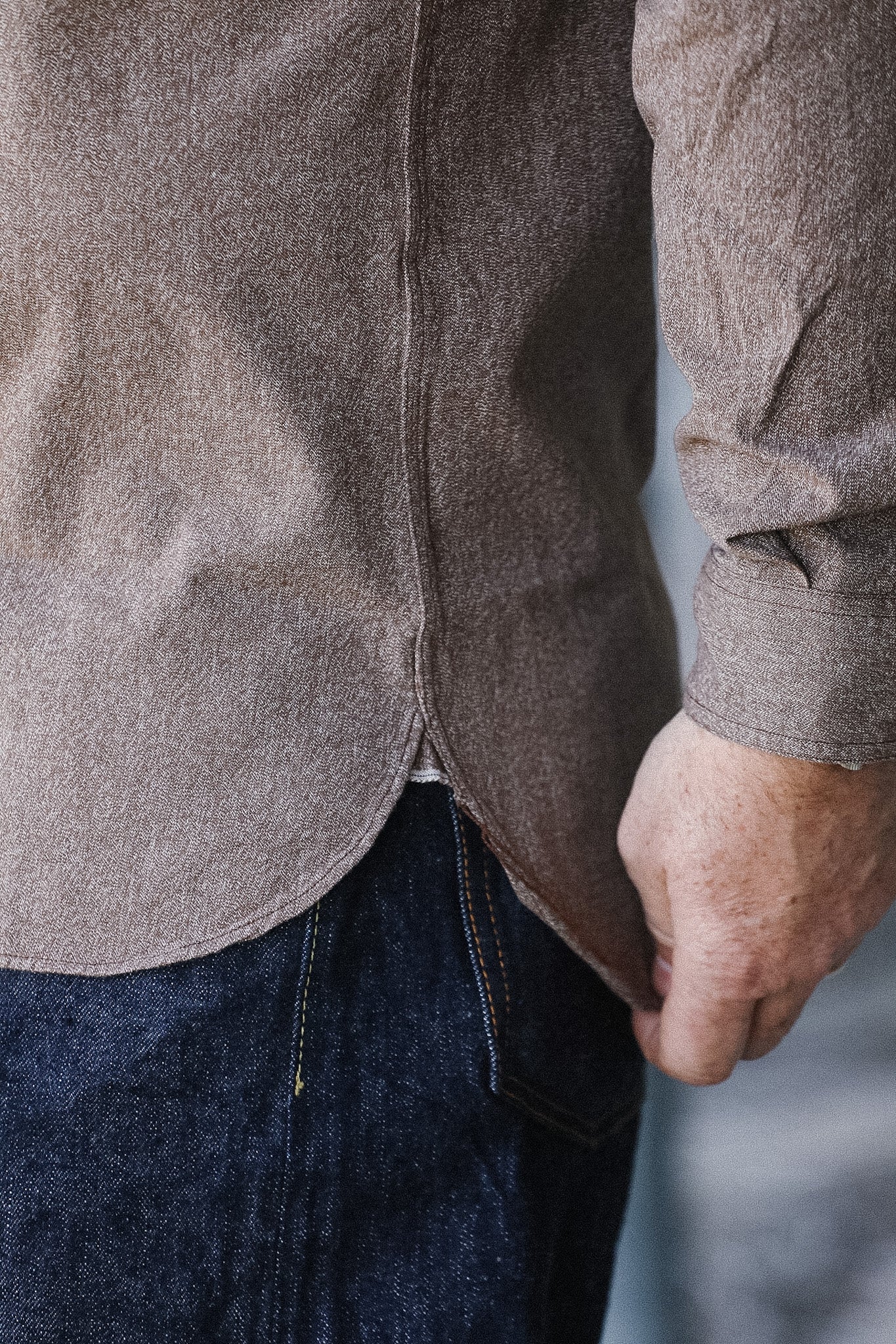Close-up of a person wearing a brown shirt and dark jeans against a light background