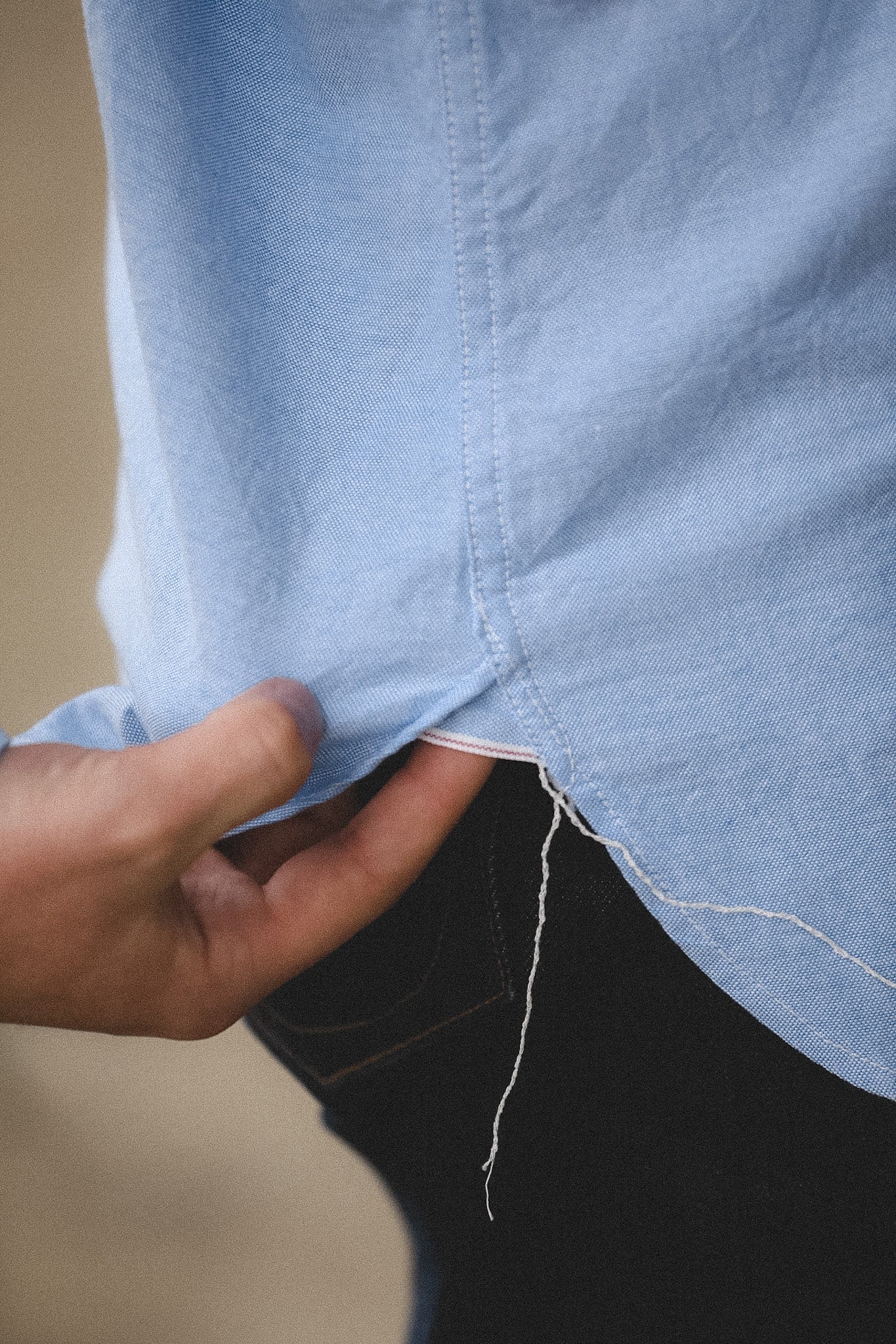 Close-up of a person adjusting a light blue shirt with a blurred background