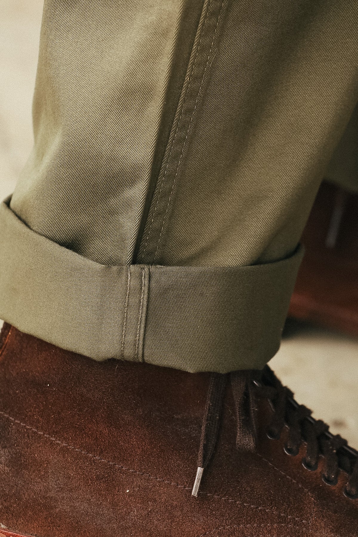 Close-up of olive green trousers with a rolled cuff, paired with a brown suede lace-up boot.