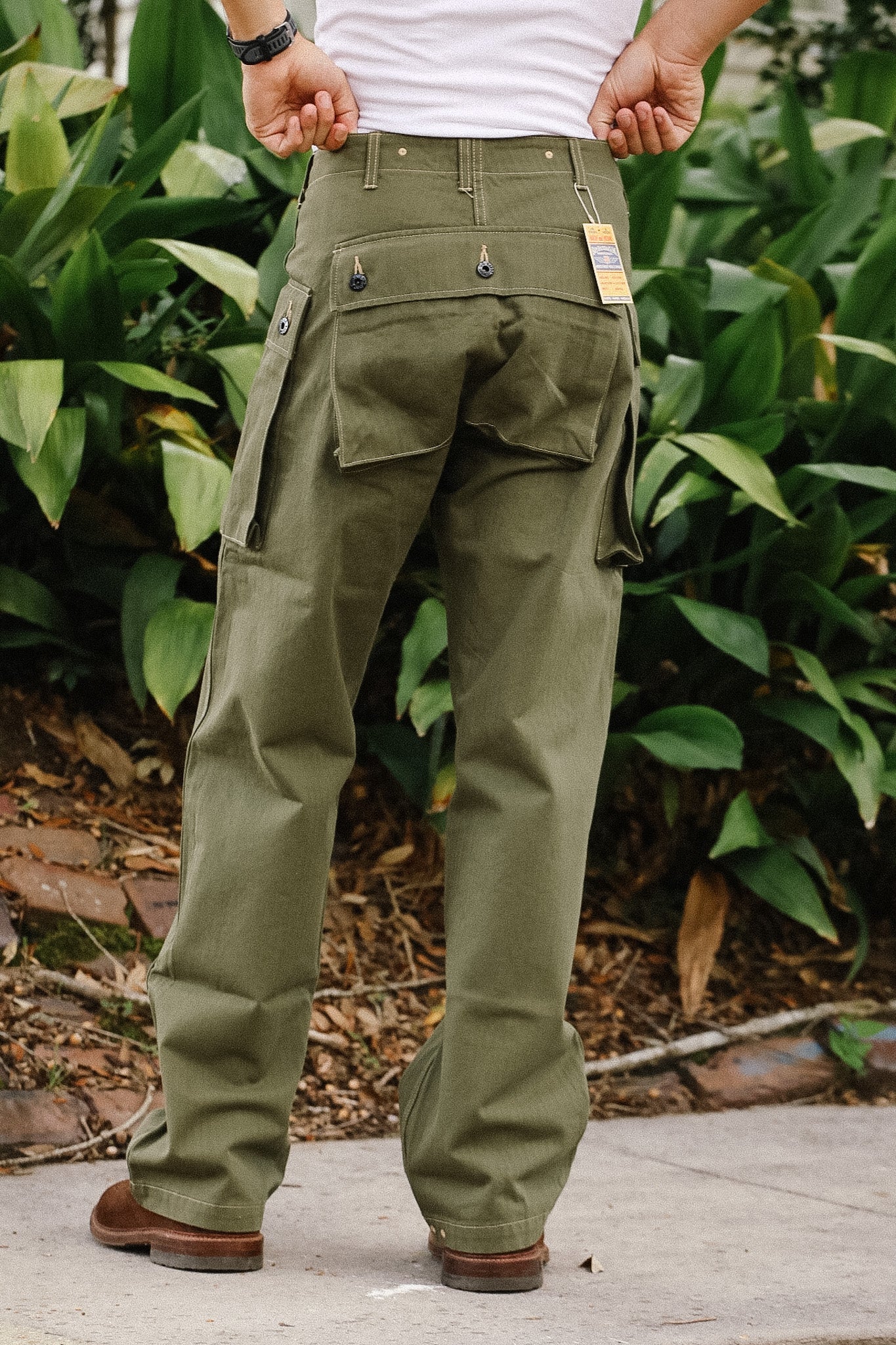 Person wearing olive green cargo pants with a white shirt and brown shoes, standing outdoors.