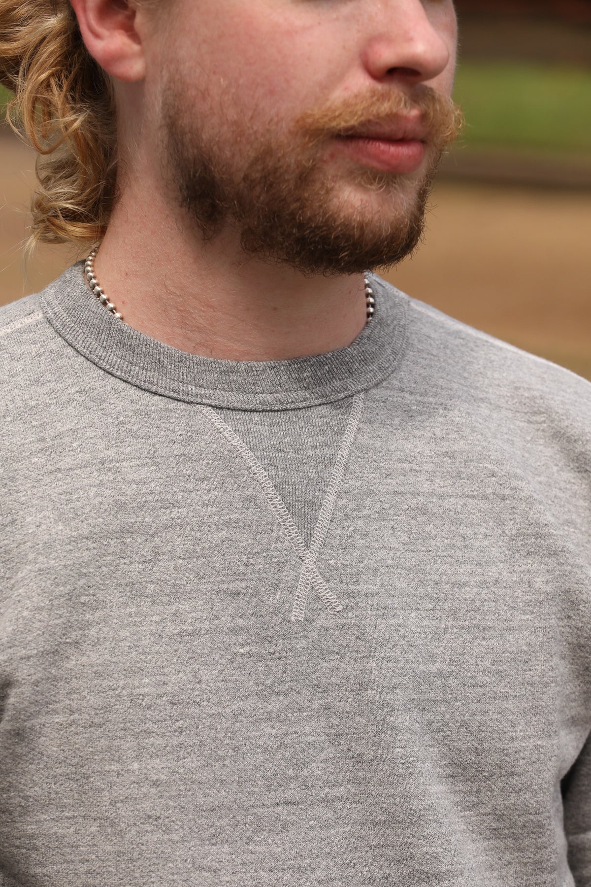 Close-up of a man wearing a heather gray crewneck sweatshirt, showing the texture of the fabric and the V-neck seam detail.