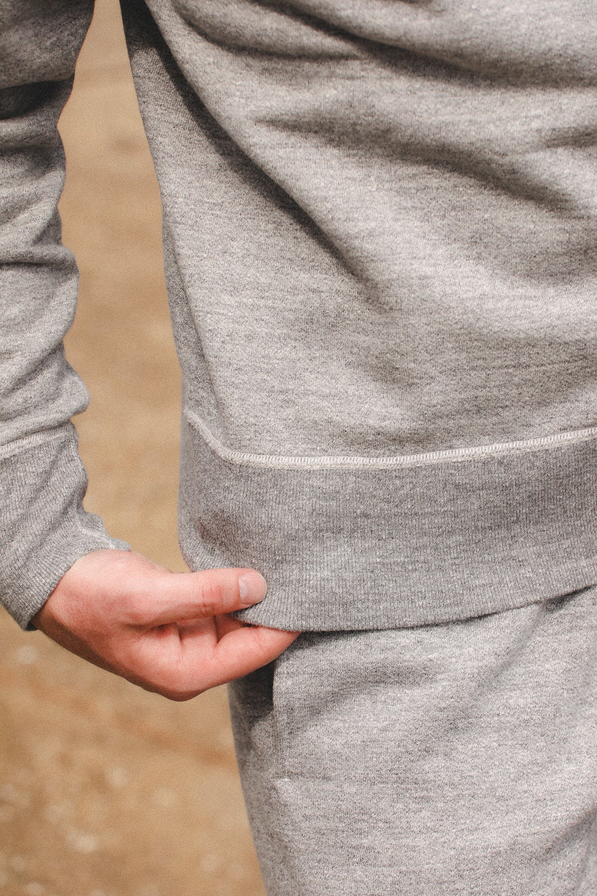 Close-up of a person wearing a heather gray fleece or sweatshirt, showing the ribbed cuff on the sleeve and the side pocket area, with a hand pulling the fabric slightly outward.