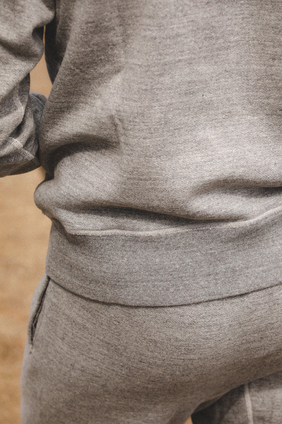 Close-up of a person wearing a heather gray sweatshirt and matching sweatpants, focusing on the ribbed waistband and fabric texture.