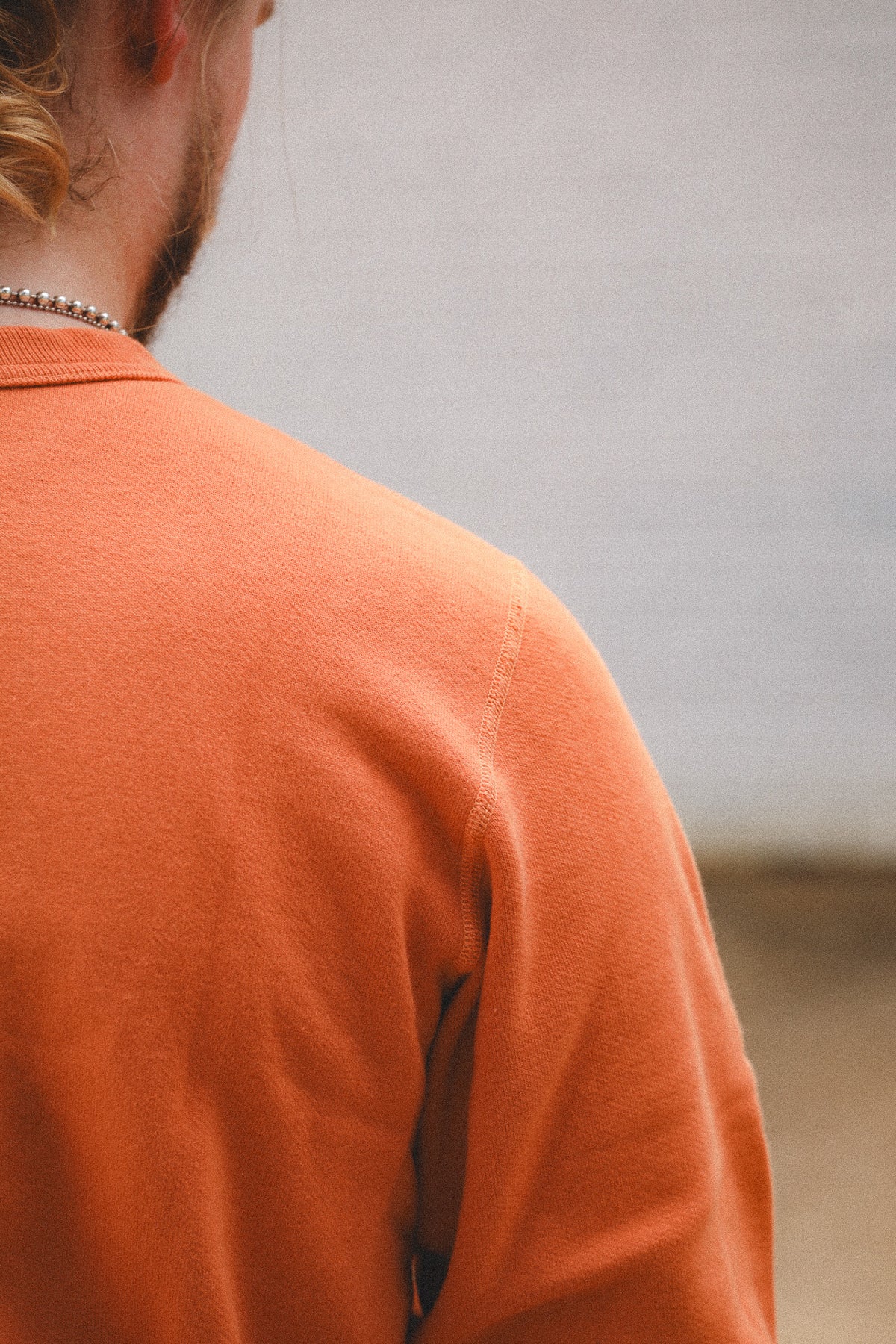 Close-up back view of a person wearing a textured orange crewneck sweatshirt, showing the shoulder seam and neck area.